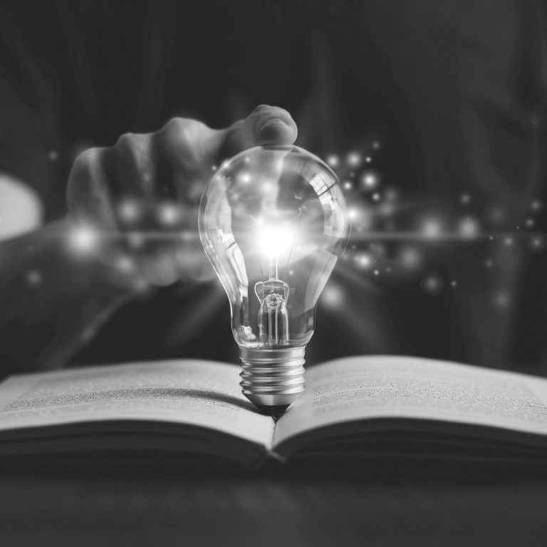un doigt qui touche une ampoule illimunée, déposée sur un livre ouvert.