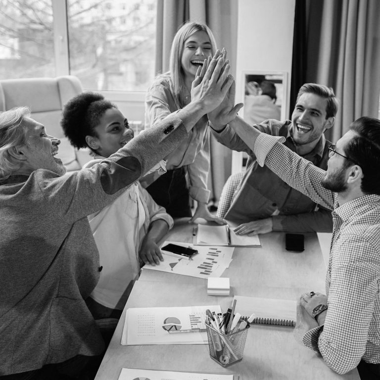 Une équipe de travail assise au tour d'une table dans un bureau, qui se tappe dans les maisons pour ce féliciter.